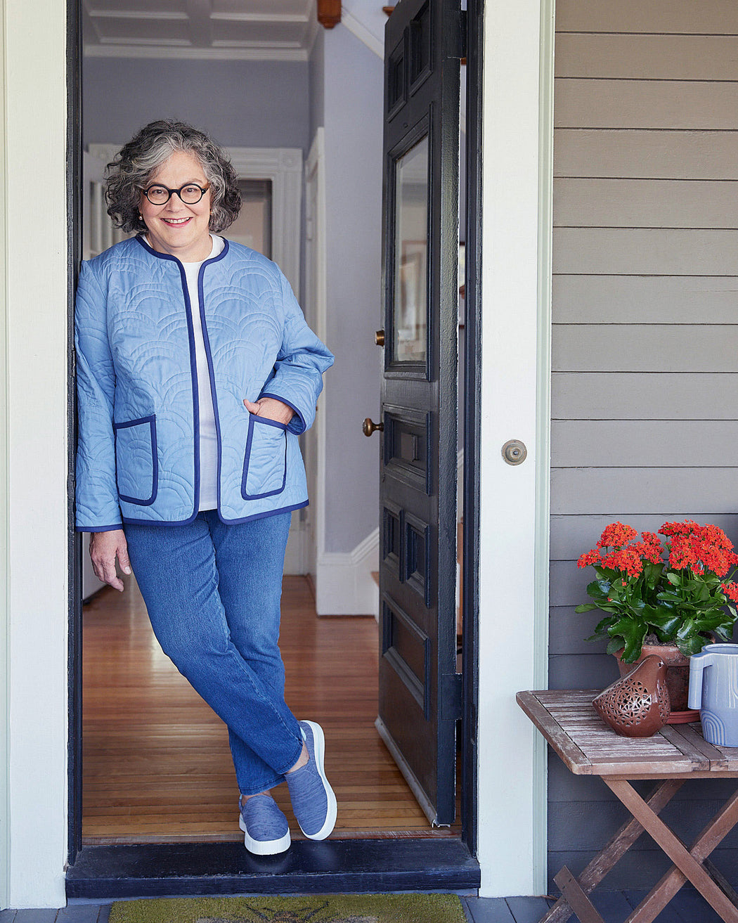 Woman in a blue outfit standing in a doorway with a plant on a table to her right. This jacket is the Fairfax Quilted Jacket sewing pattern from "Sewing the Curve" by Jenny Rushmore.