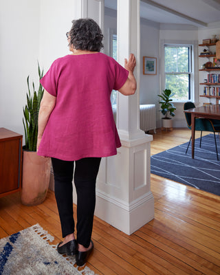 Woman in a pink shirt standing in a home interior, looking into another room. This top is the Montvale Dress & Tunic sewing pattern from "Sewing the Curve" by Jenny Rushmore.