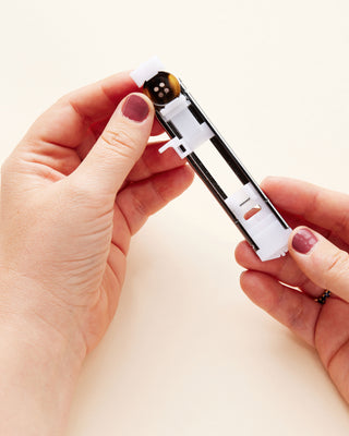 Close-up of a person holding a buttonhole foot for a sewing machine on a white background