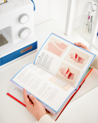 Open book with sewing instructions on a white table with sewing equipment. This book is Sewing the Curve by Jenny Rushmore.