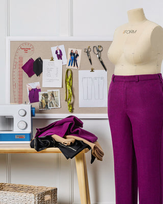 Mannequin wearing purple pants next to a sewing machine and materials on a table.
