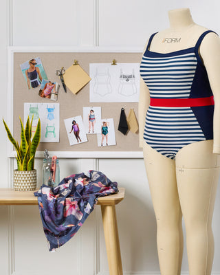 Mannequin wearing a striped swimsuit with a design board in the background. This swimsuit is the Ipswich Swimsuit sewing pattern from Cashmerette.