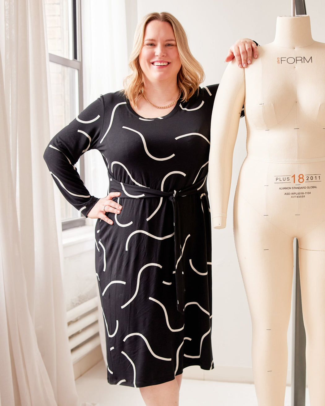 Woman in a black dress standing next to a mannequin in a well-lit room. This is the Pembroke Dress sewing pattern from Cashmerette.