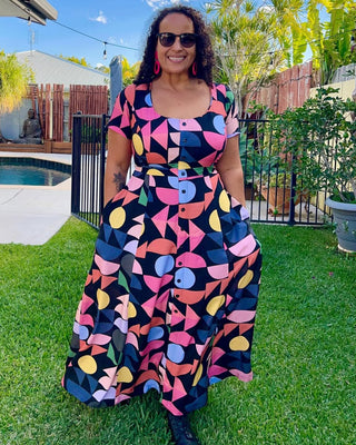 Woman wearing a colorful dress standing in a backyard with a pool and garden. This is the Hampden Dress sewing pattern from Cashmerette.