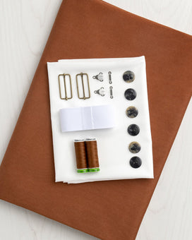 Crafting supplies including thread, buttons, and hardware on a brown fabric background. This is the Osgood Skirt kit from Core Fabrics.