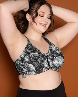 Woman wearing a black floral sports bra and black leggings against an orange background. This is the Somerville Sports Bra sewing pattern from Cashmerette.