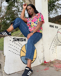 Woman sitting on a wall with graffiti, wearing a floral shirt and blue jeans. This is the Montrose Top sewing pattern from Cashmerette.