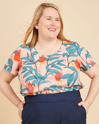Woman wearing a colorful floral top and navy wide-leg pants on a beige background. This is the Montrose Top sewing pattern from Cashmerette.