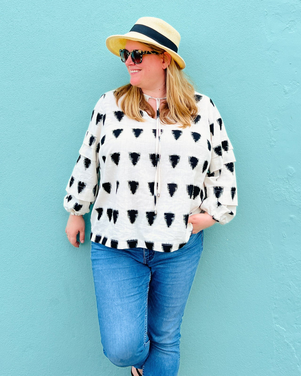 Woman wearing a patterned blouse, sunglasses, and a hat against a light blue background. This top is the Alton Blouse sewing pattern from Cashmerette.