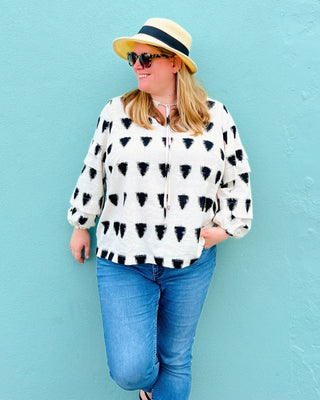 Woman wearing a patterned blouse, sunglasses, and a hat against a light blue background. This top is the Alton Blouse sewing pattern from Cashmerette.