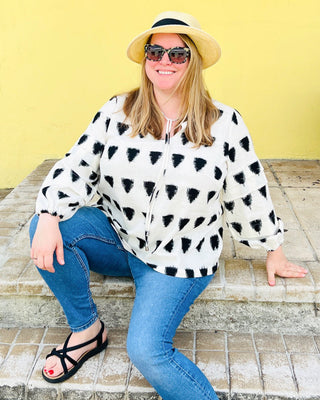 Woman wearing a black and white patterned shirt blue jeans, and a straw hat against a yellow wall. This top is the Alton Blouse sewing pattern from Cashmerette.