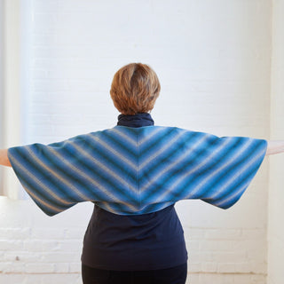 Person wearing a blue and gray striped shawl against a white background. The topper is the Caroll Shrug sewing pattern from Cashmerette.